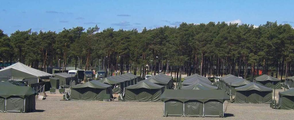 Military tent and container based infrastructure on sandy ground in front of a forest 