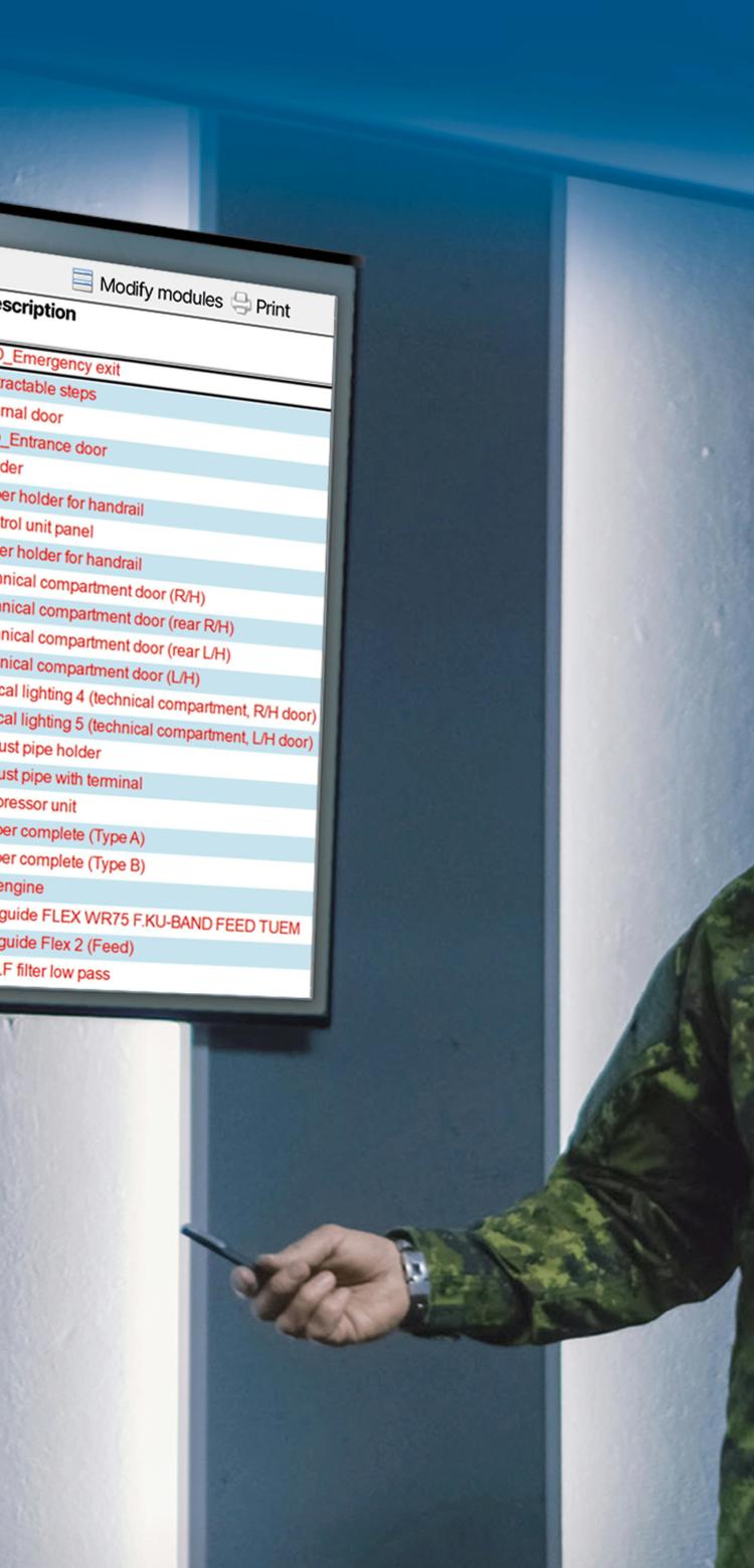 A Soldier in a modern operation centre standing next to a screen displaying a table of SMaC. Additional screens and soldiers working on computers are visible in the background.
